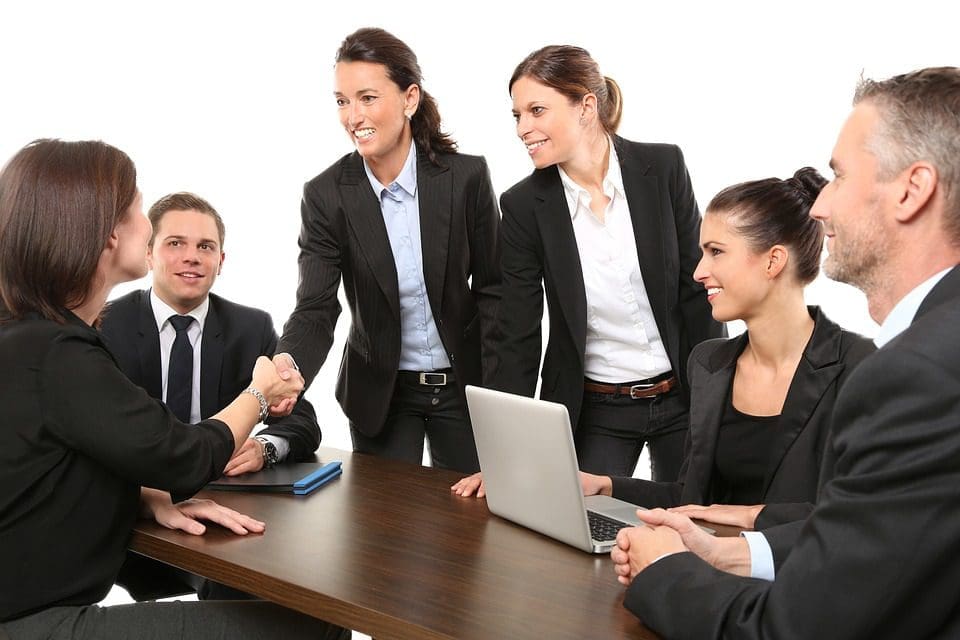 6 empleados en una mesa y dos de ellos estrechando manos